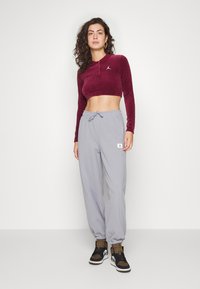 Top corto acanalado burdeos con cuello, combinado con pantalones de chándal gris claro que cuentan con una cinturilla elástica y un parche de logo lateral.