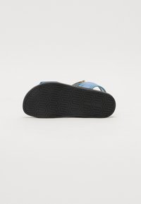 Blauwe sandaal met een gestructureerde zwarte rubberen zool, verstelbare bandjes en een glad bovenmateriaal. Bevat een geometrisch patroon op de zool.