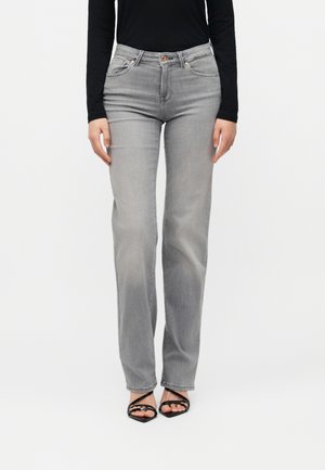 Kvinde iført grå lige jeans med høj talje, sort langærmet top og sorte strop-sandaler med åben tå, stående frontvendt.