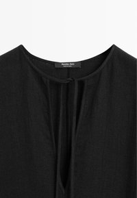 Blouse en tissu noir texturé avec encolure ronde et détail noué à l'avant, portant une étiquette Massimo Dutti à l'intérieur du col.