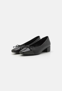 Svarta ballerinas med en blank, tåcap-finish. Har en rosettdetalj och en låg, kvadratisk klack. Slät lädertextur genom hela skon.