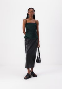 Green satin peplum top, black leather midi skirt, chunky black sandals, and a small black handbag. Minimalist design, smooth texture.