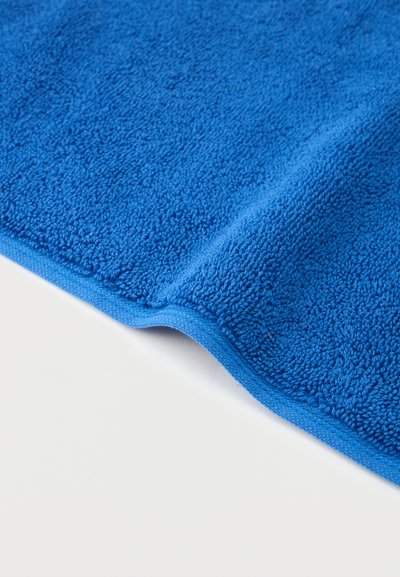 Φωτεινή μπλε πετσέτα από περκάλι με ραμμένα άκρα, μερικώς διπλωμένη σε λευκή επιφάνεια.