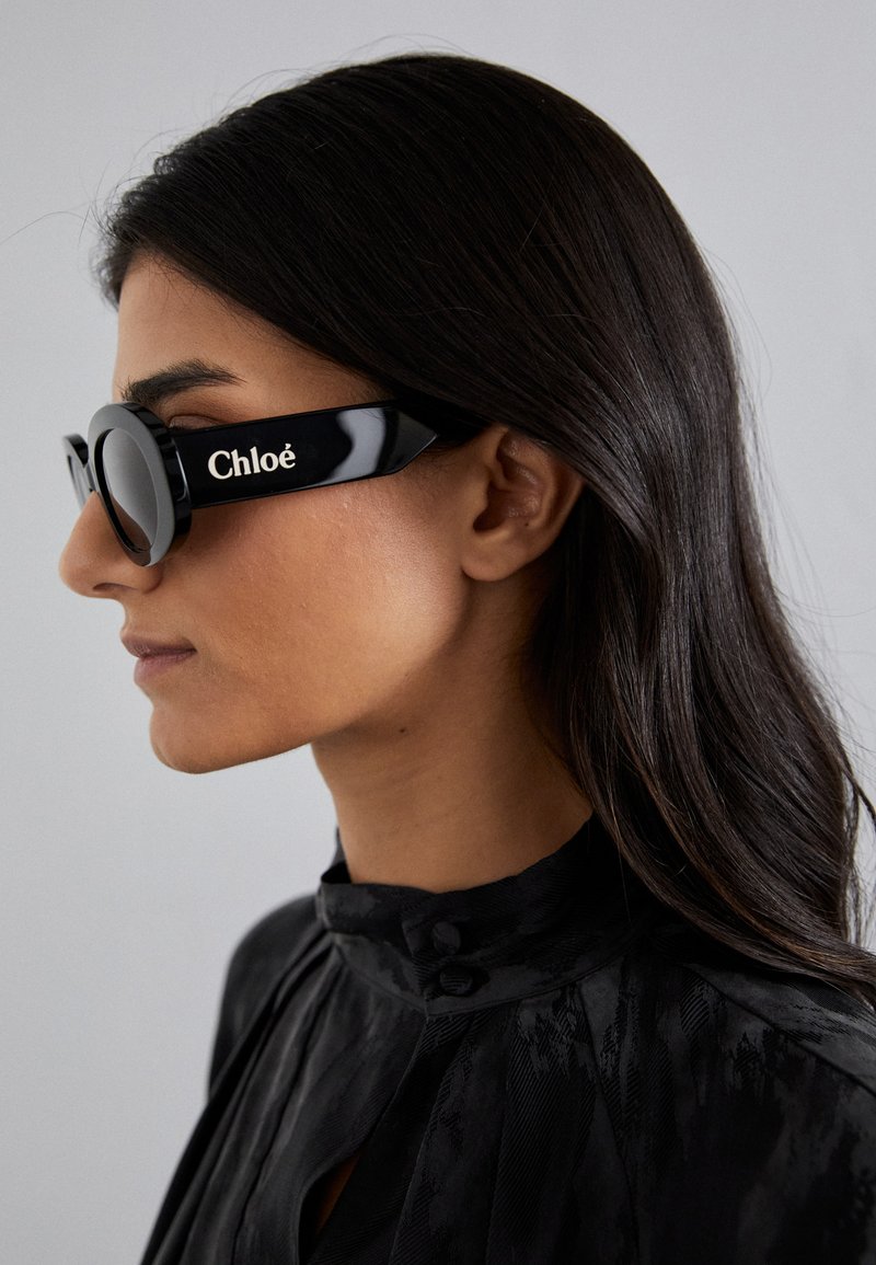 Gafas de sol negras con lentes redondos y montura angular y audaz que presentan la marca "Chloé" en blanco en el lateral. Acabado suave y brillante.