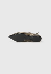 Chaussure à bout pointu avec une finition en bronze métallique, semelle noire et une fine lanière. Texture lisse avec une apparence polie et un minimalisme dans les détails.