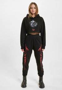 Black cropped hoodie with a bear graphic and "Thug Life" text, paired with black joggers featuring red flame patterns and elastic cuffs.