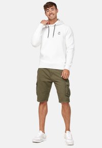 Witte hoodie met een logo, zwarte trekkoordjes en geribbelde manchetten, gecombineerd met olijfgroene cargoshorts met zijzakken, gedragen met witte sneakers.