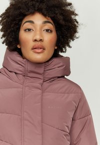 Helle rosa Steppjacke mit hohem Kragen, gesteppter Textur und dezenter Markenkennzeichnung. Glattes Material mit modernem, strukturiertem Design.