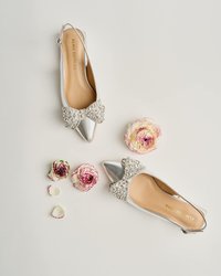 Balinais argentés avec un bout pointu, agrémentés d'un grand nœud orné de bijoux. Cuir lisse avec un intérieur doux. Fleurs blanches et roses à proximité.
