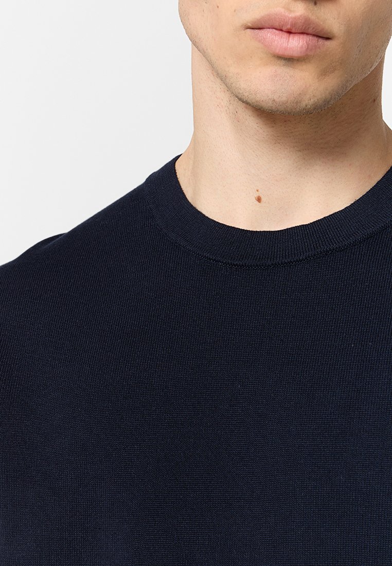 Pull à col rond en tricot bleu marine, fabriqué en tissu texturé côtelé, présentant un col net et une finition lisse. Vue en gros plan.