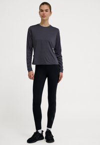 Szara, długosleeve'owa koszulka sportowa, dopasowane czarne legginsy z teksturowanym wzorem, zestawione z czarnymi butami sportowymi i białymi skarpetkami.