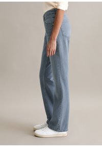 Lichtblauwe rechte jeans van denimstof, met een hoge taille, achterzakken en een nette afwerking. Gecombineerd met witte sneakers.