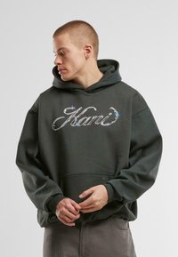 Dark green hoodie featuring a front pocket and a large reflective logo. Designed with a classic fit and ribbed cuffs for comfort.