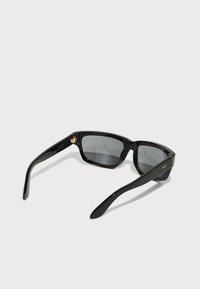 Gafas de sol negras con montura rectangular, lentes grises y acentos de hardware dorado. Hechas de plástico brillante con patas curvas y elegantes.
