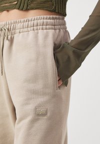Beige Sweatpants mit strukturiertem Finish, elastischem Bund und Seitentaschen. Verfügt über ein kleines Logopatch mit einem Sterneemblem.