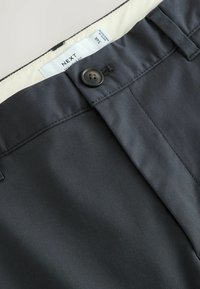 Pantalon gris foncé avec fermeture par bouton et étiquette intérieure visible indiquant la taille 34R et la marque NEXT.