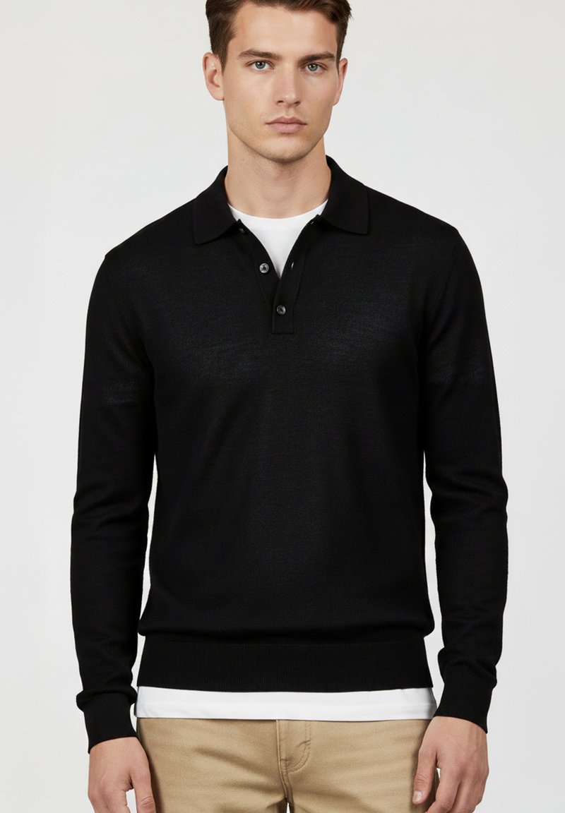 Maglione polo nero a maniche lunghe con collo a polo, patta con tre bottoni e polsini a coste. Indossato sopra una t-shirt bianca.