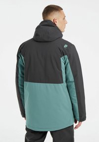 Herrejakke i sort og teal farveblokke, med hætte, lange ærmer og blød tekstur, samt logoaccents på skulderen.