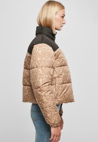 Puffjakke har et brunt og beige damaskmønster, kontrasterende mørk krage, quiltet design og elastiske mansjetter.