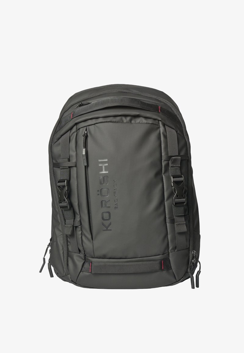 Sac à dos noir KORÖSHI avec plusieurs compartiments zippés, bretelles réglables et boucles sur fond blanc.