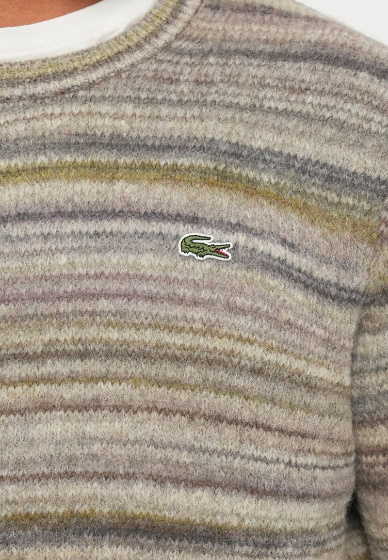 Knit sweater in beige with textured stripes in gray, green, and brown. Features a small green crocodile logo on the chest.
