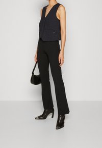 Marinblå randig knälång väst med V-ringning och knappstängning, kombinerad med svarta utsvängda byxor och klackiga ankelstövlar. Svart handväska ingår.