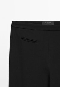 Schwarze Hose aus glattem Stoff mit einer kleinen Paspeltasche an der Seite und einem Etikett mit der Aufschrift "Massimo Dutti" im Bundinnenseite.