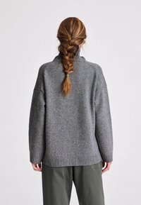 Suéter gris de punto con cuello alto y ribete acanalado, con hombros relajados y textura suave. Combinado con pantalones cargo sueltos.