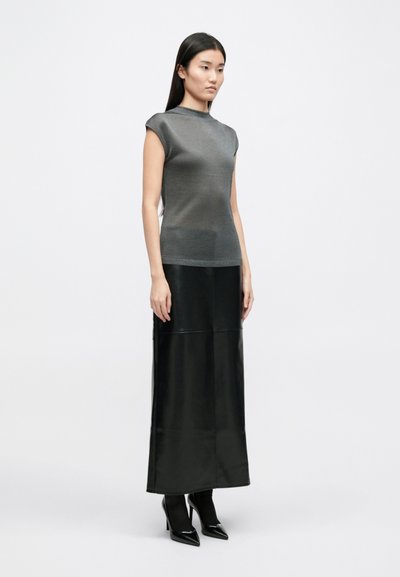 Szürke, testhezálló top, rövidujjakkal, hosszú, fekete bőrszoknyával és fekete magassarkú cipővel párosítva, fehér háttér előtt.