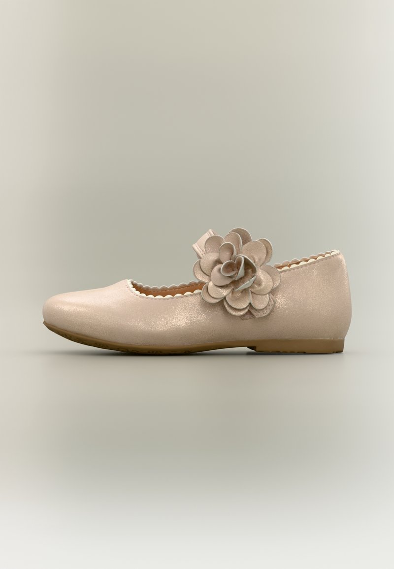 Chaussure plate beige avec bord festonné et grande fleur décorative sur la bride traversant le cou-de-pied, affichée sur un fond neutre.