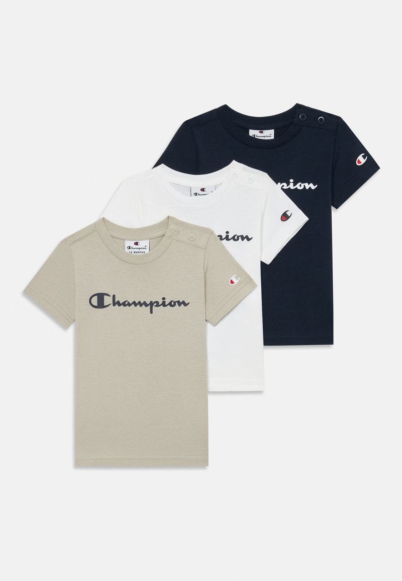 Trois t-shirts à manches courtes en beige, blanc et bleu marine, avec des cols ronds, un logo en écriture et des accents de boutons-pression sur les épaules.