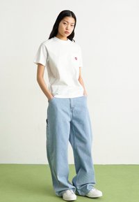 Bílý tričko s krátkým rukávem a kapsou s designem červených rtů, doplněné světle modrými oversized džíny a bílými teniskami.