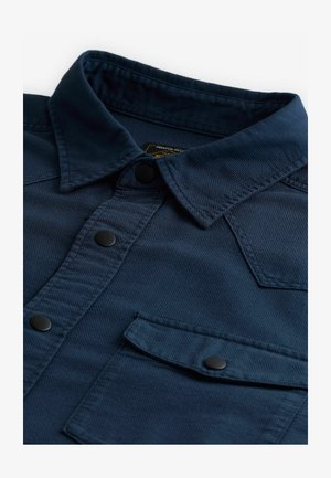 Navy blue shirt with a pointed collar, textured fabric, and black snap buttons. Features a chest pocket with a button closure.