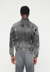 Juoda ir pilka džinsinė striukė su išblukinta apdaila. Turi klasikinį apykaklę, sagų užsegimą ir ilgus rankovius. Dėvima su derančiomis pilkomis kelnėmis.