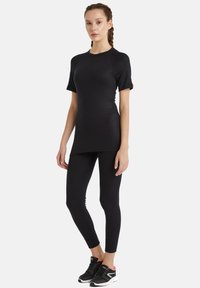 Svart träningsset bestående av en figurnära kortärmad topp och tights. Slät tyg, minimalistisk design och subtilt röd accent på ärmen.