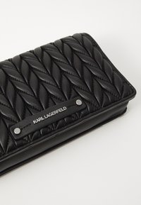 Portafoglio in pelle nera trapuntata con una texture intrecciata in rilievo e una placca del logo in tono argento con due borchie metalliche.