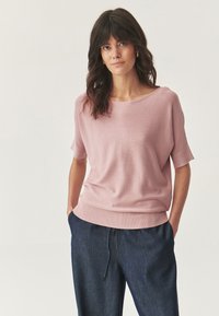 Lichtroze sweater met korte mouwen en een brede halslijn, geribbelde zoom en een zachte textuur, gecombineerd met donkere denimbroeken.