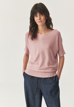 Light pink short-sleeve sweater with a wide neckline, ribbed hem, and soft texture, paired with dark denim trousers.