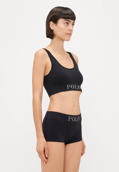 Črna bombažna braletta s širokim pasom, na katerem je logo "POLO", kombinirana s črnimi spodnjicami tipa boyshort, oboje gladke teksture in preprostega dizajna.