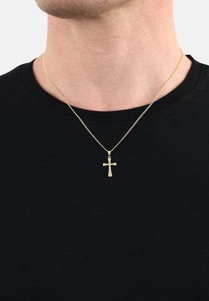 Collier en croix en or sur une fine chaîne, porté par-dessus un t-shirt noir à col rond. La croix présente un design simple et plat sans embellissements.