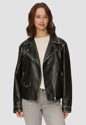 Veste de motard en cuir noir avec des zips métalliques, un col en revers et des détails en couture argentée. Portée sur une chemise de couleur claire.