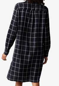 Svart och vit rutig klänning med långa ärmar, något lös passform, knappmanchetter och en ryggparti detaljer. Mjuk textur, knälång design.