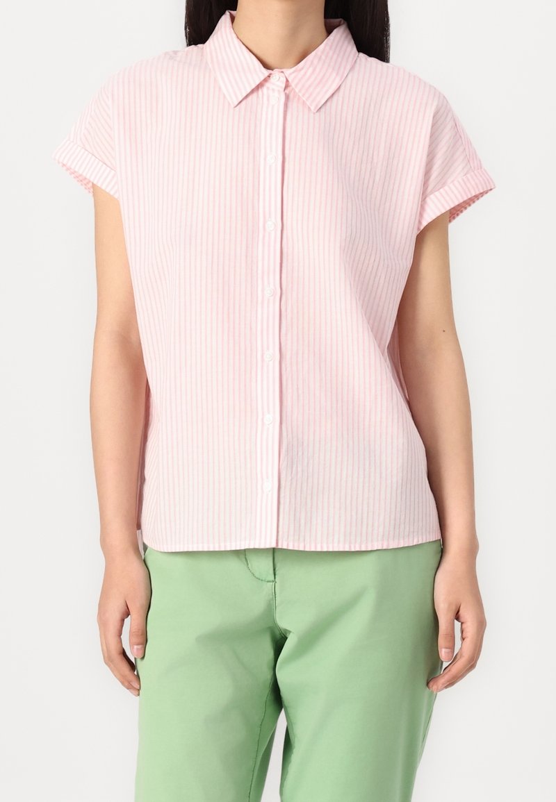 Chemise à manches courtes à boutons de couleur rose clair avec de fines rayures blanches. Elle présente un col classique et une coupe décontractée, associée à un pantalon vert.