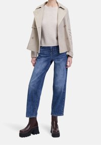 Beige double-breasted trench coat over a cream knit sweater, paired with high-waisted blue wide-leg jeans and brown platform boots.