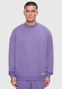 Lila Sweatshirt mit Rundhalsausschnitt, gesenkten Schultern und ribbed Bündchen. Mit einem strukturierten Logo-Patch an der unteren Seite. Weicher Stoff.