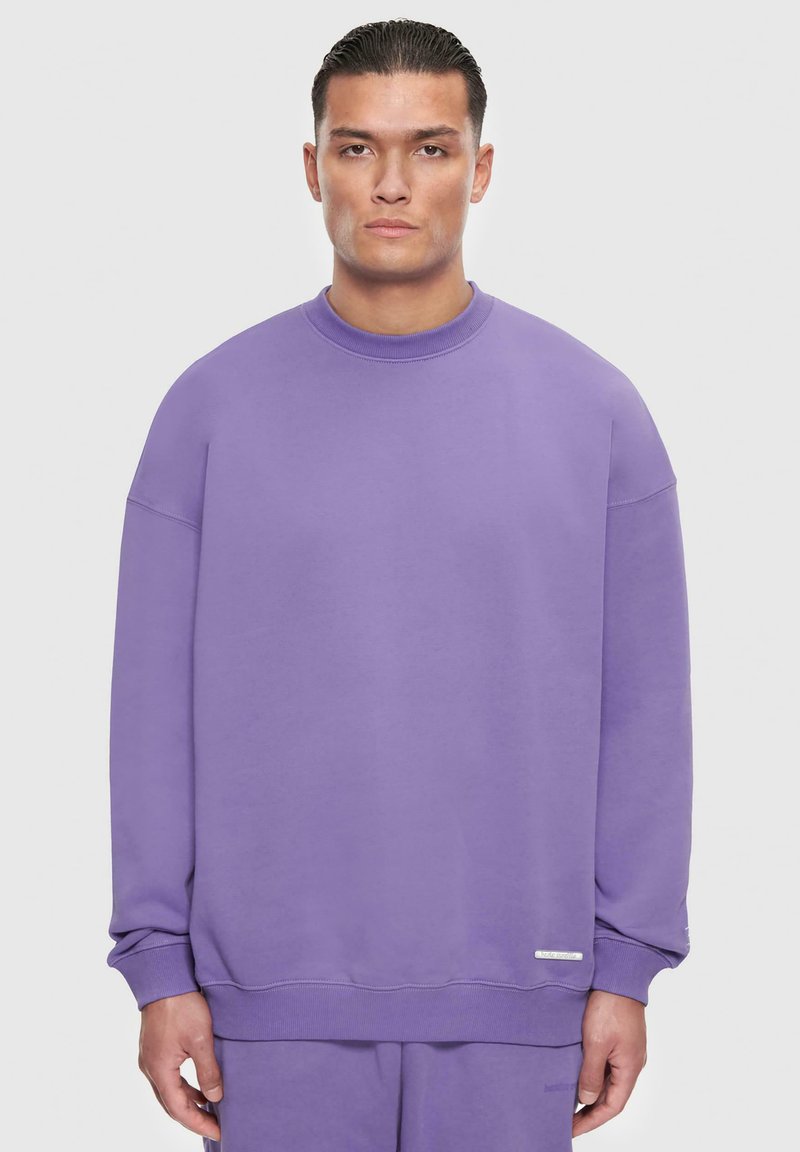 Lila Sweatshirt mit Rundhalsausschnitt, gesenkten Schultern und ribbed Bündchen. Mit einem strukturierten Logo-Patch an der unteren Seite. Weicher Stoff.