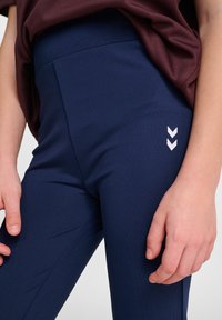 Marina leggings tillverkade av elastiskt tyg, med en mjuk yta, hög midja och en vit chevron-logotypaccent på låret.