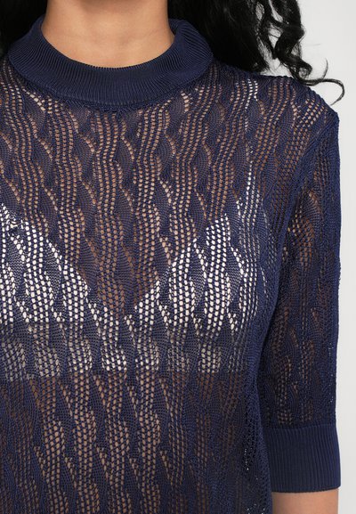 Suéter de punto azul marino con cuello alto, que presenta un tejido abierto con patrones y mangas cortas, mostrando un diseño texturizado y ligero.