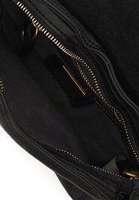 Interno in suede nero di una borsa, con un comparto con zip e hardware in tono oro, cuciture a vista e fodera in tessuto.