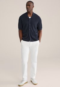 Marineblå kortærmet cardigan med struktureret strik, knapper foran, to forlommer, kombineret med hvide bukser og lyse sneakers.